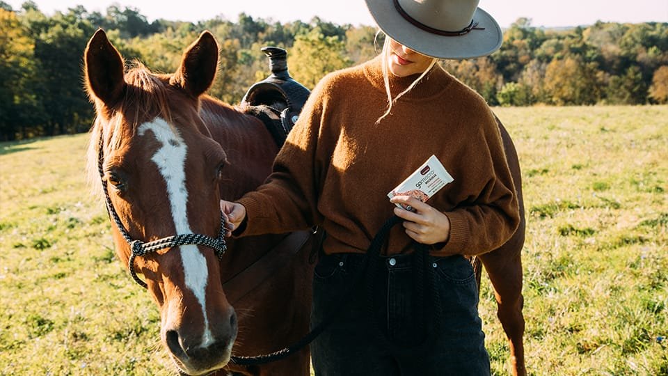 Woman holding a GoMacro MacroBar next to horse