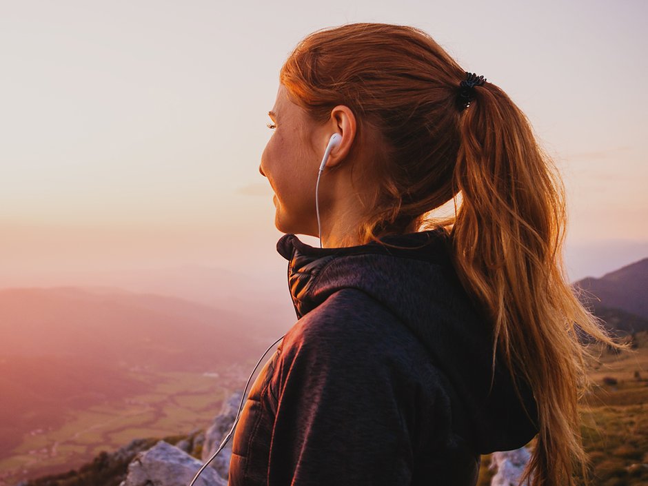 Woman looking out over a sunset with earbuds in