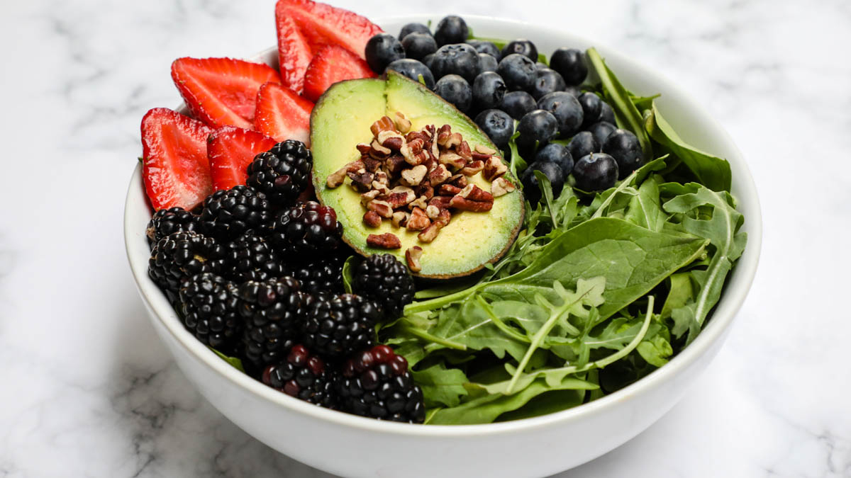 Spinach salad topped with berries, avocado, and pecans