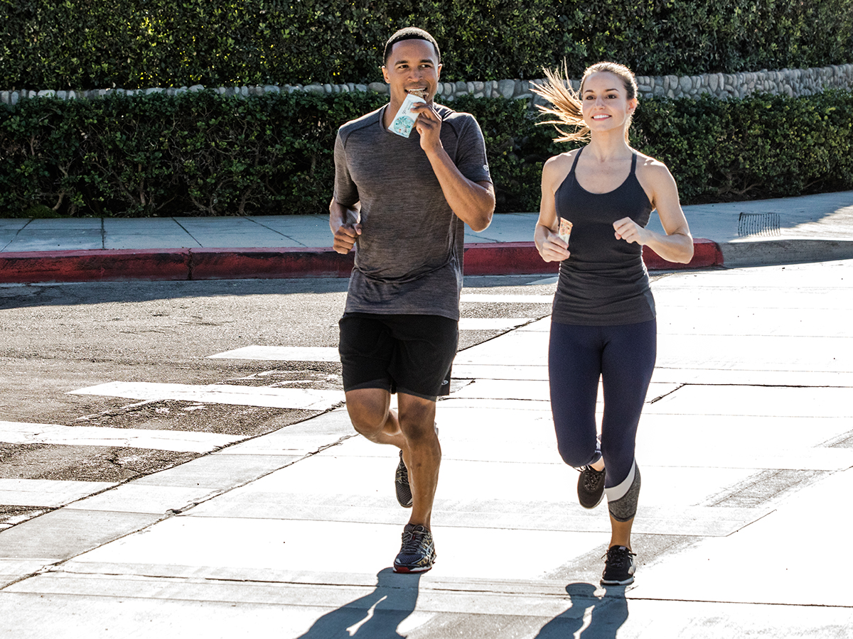 Man and woman jogging, man is eating a GoMacro MacroBar
