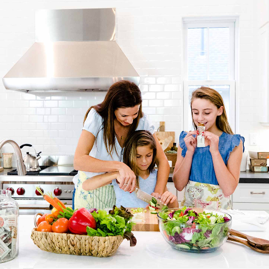 Mom in kitchen with daughters, oldest daughter is eating a GoMacro MacroBar